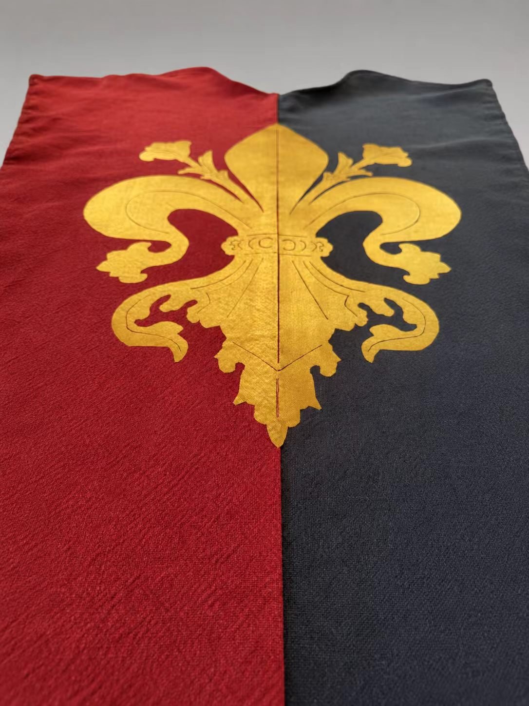 Red and black medieval cosplay tabard detail with gold fleur-de-lis motifs.