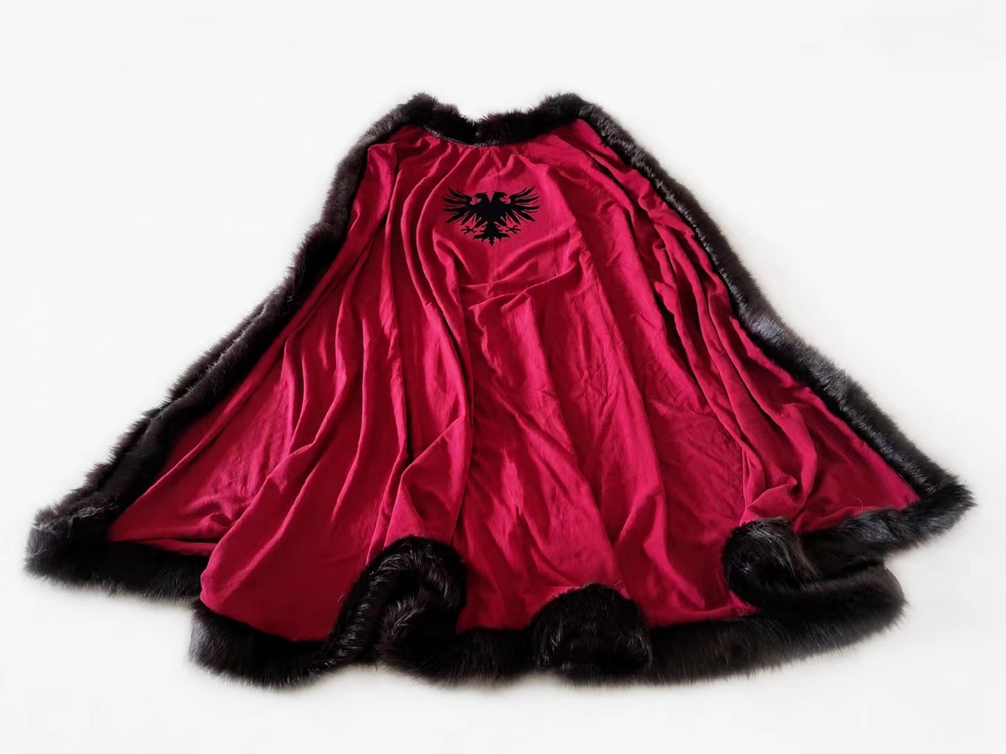 Red and black medieval cosplay cloak with fur-like edge laid flat.