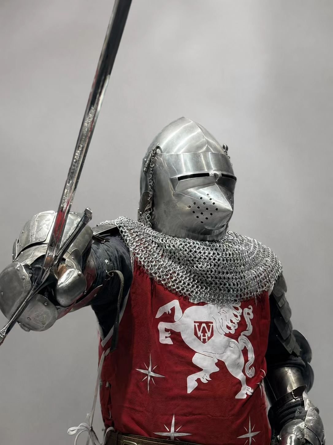 Medieval knight cosplay armor with red surcoat, sword, chainmail, and helmet.