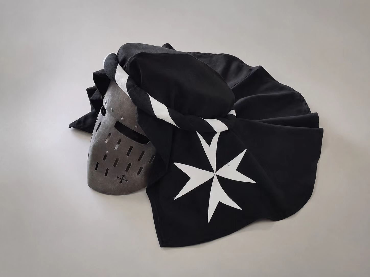 Black and white medieval knight helmet with cross headscarf cover.