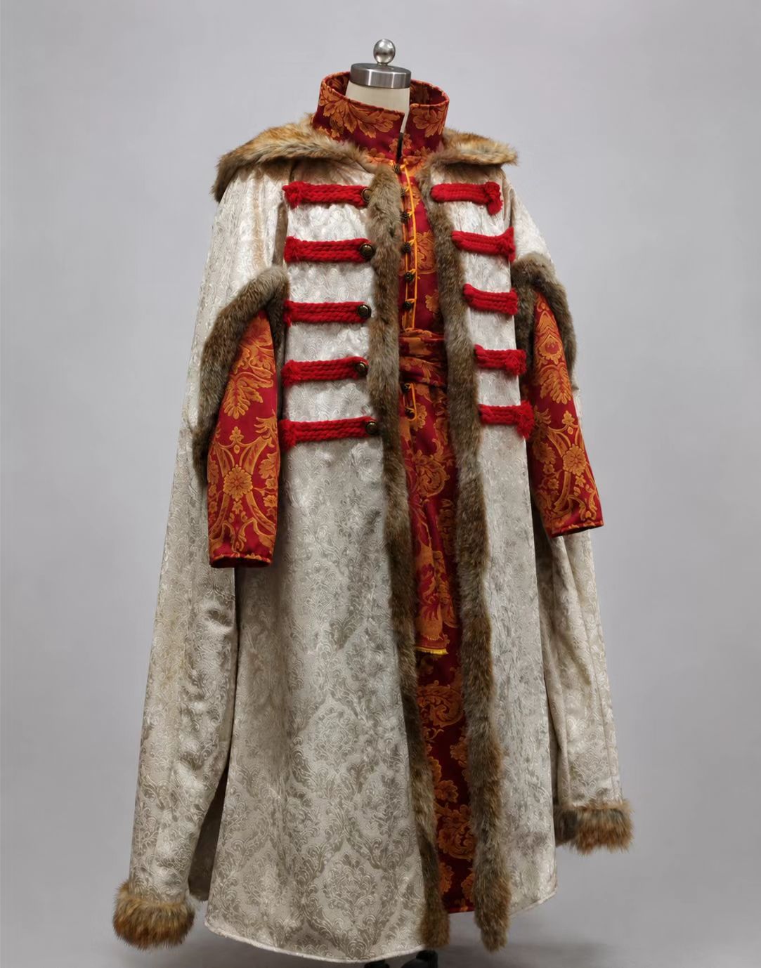 16th-17th century Polish noble robe set with red-gold jacquard inner robe, pale outer robe, red cord closures, brass buttons, and fur-trimmed collar and edges.