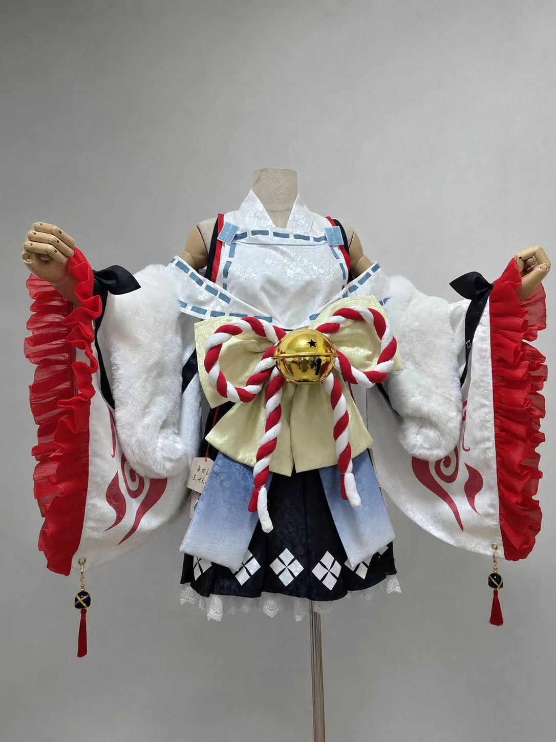 Premium handmade Japanese miko cosplay costume with red ruffle wide sleeves, faux-fur sleeve ornaments, red-and-white cord knots, gold bells, and layered skirt styling.